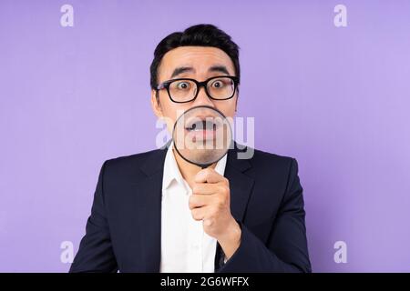 Uomo d'affari in tuta con lente d'ingrandimento, isolato su sfondo viola Foto Stock