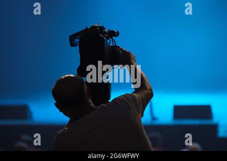 Silhouette di un cameraman con una videocamera impegnata in riprese video nella sala. Foto Stock