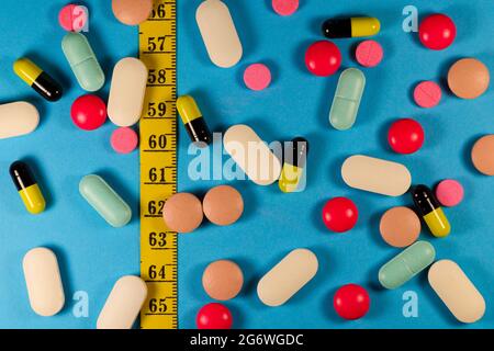 Varietà di pillole e capsule con nastro di misurazione su blu Foto Stock