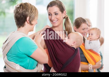 Il gruppo di donne a imparare a utilizzare imbracature bambino per madre-bambino l'incollaggio Foto Stock