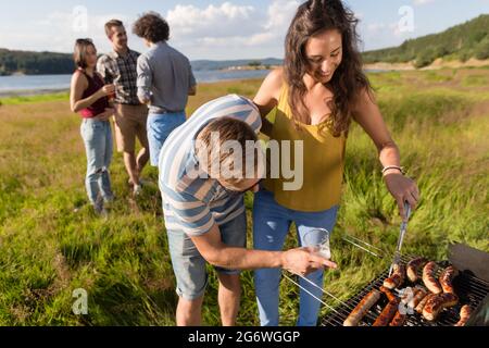 Giovane uomo e donna grigliare salsicce sul barbecue grill al partito nella natura Foto Stock