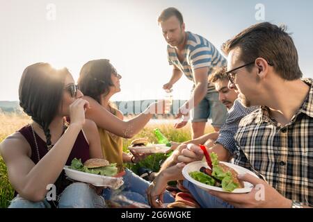 I giovani aventi estate picnic barbecue e mangiare insieme seduta in erba Foto Stock