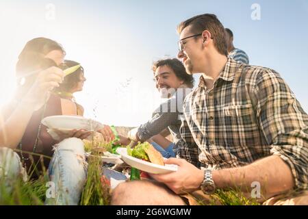 I giovani aventi estate picnic barbecue e mangiare insieme seduta in erba Foto Stock