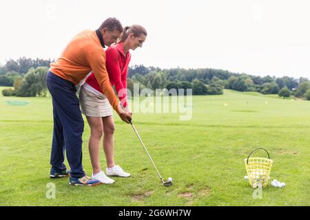 Istruttore di golf maschile insegnando giocatore di golf femminile per prendere un tiro Foto Stock