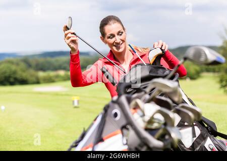 Close-up di sorridere giocatrice scegliendo golf club dal sacco Foto Stock