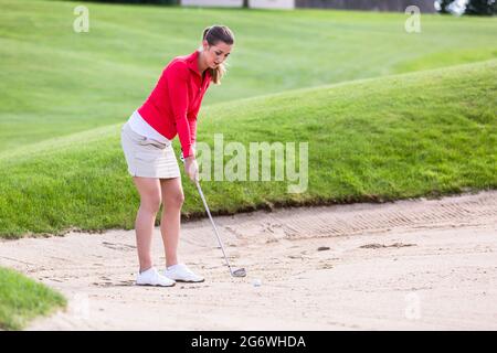 Golfer femminile che si prepara per scalpellare la palla fuori dal bunker in corso Foto Stock