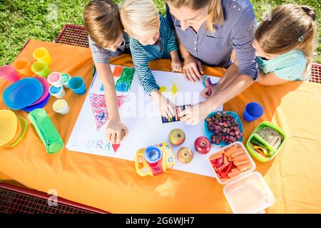 Scolare e scolari pittura durante la pausa pranzo con frutti e sandwich Foto Stock
