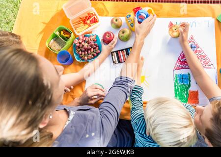 Scolare e scolari pittura durante la pausa pranzo con frutti e sandwich Foto Stock