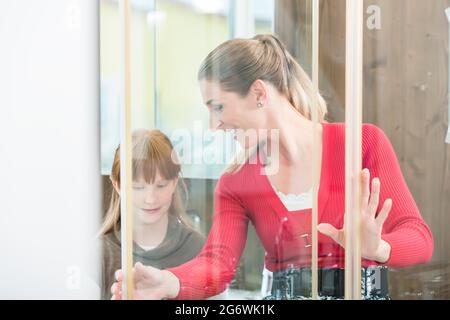 Donna allegra con sua figlia che guarda una cabina doccia nello showroom di un negozio di articoli sanitari con moderni impianti da bagno in vendita Foto Stock