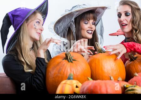 Tre giovani e belle donne che indossano divertente festa costumi mentre agiscono come le streghe, unendo le loro forze dannoso di Halloween Foto Stock
