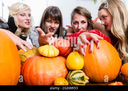 Tre giovani e belle donne che indossano divertente festa costumi mentre agiscono come le streghe, unendo le loro forze dannoso di Halloween Foto Stock