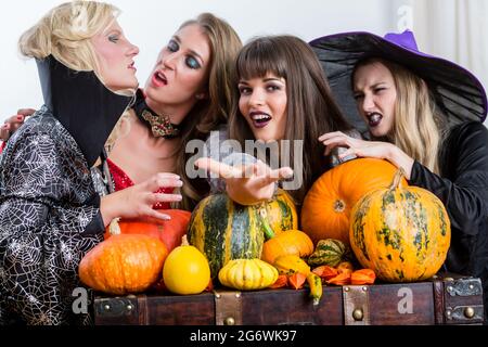 Quattro allegro belle donne durante la tostatura celebrare Halloween insieme durante la festa in costume al chiuso in una sala decorata Foto Stock