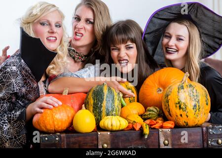 Quattro allegro belle donne durante la tostatura celebrare Halloween insieme durante la festa in costume al chiuso in una sala decorata Foto Stock