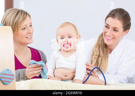 Ritratto di una bella e sana bambina guardando la fotocamera con i suoi occhi blu, mentre è seduto tra la madre e un esperto pediatra d Foto Stock