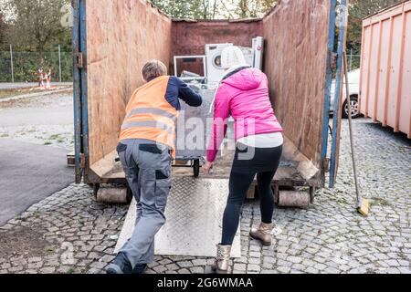 Donna e uomo dando elettrodomestici al centro di riciclaggio di una macchina di lavaggio Foto Stock