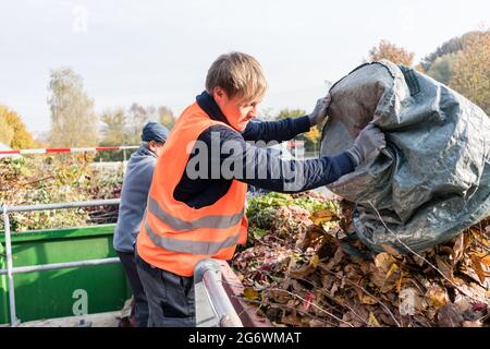 Uomo che dà rifiuti verdi in contenitore sul centro di riciclaggio all'aperto Foto Stock