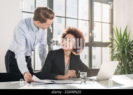 Controllo del supervisore le statistiche sulle imprese e spiegare i risultati a un collega seduto alla scrivania in ufficio Foto Stock