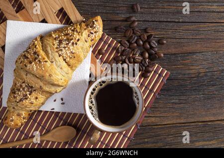 Tazza di caffè caldo e croissant con semi di sesamo per colazione su tavolo di legno scuro, vista dall'alto Foto Stock