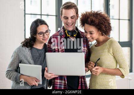Giovani allegro team di tre persone a guardare un video o cerca su una presentazione aziendale su laptop in ufficio Foto Stock