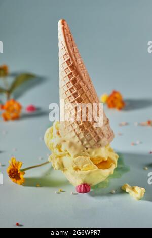 Gelato al mango con cono di cialda su sfondo blu con fiori gialli Foto Stock