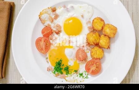 Uova fritte con prosciutto e pomodori serviti su un piatto bianco Foto Stock