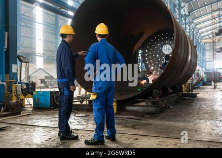 Due lavoratori esperti sorveglia la fabbricazione di un cilindro metallico all'interno di una fabbrica Foto Stock