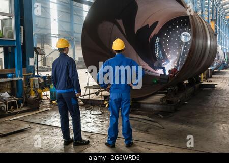 Due lavoratori esperti sorveglia la fabbricazione di un cilindro metallico all'interno di una fabbrica Foto Stock