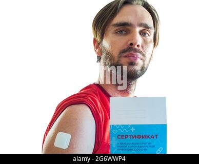 Un uomo bearded dopo la vaccinazione con un gesso incollato sulla sua spalla tiene in mano un certificato di vaccinazione. Traduzione: Certificato di vaccinazione Foto Stock