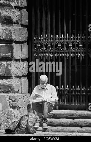 Un anziano si siede a leggere un nuovo giornale fuori dalla biblioteca Radcliffe Camera, università di Oxford, Inghilterra. Foto Stock