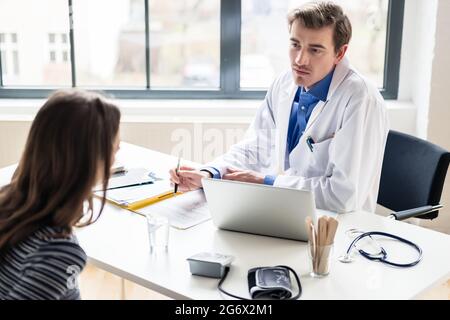 Vista ad alto angolo di un giovane medico che ascolta il suo paziente con rispetto e dedizione, durante una consultazione privata nell'ufficio di un moderno farmaco Foto Stock