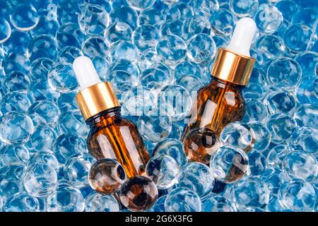 Immagine mockup di due flaconi contagocce con olio cosmetico di erbe naturale organico su sfondo blu di palline di gel d'acqua. Composizione trendy della vita still con Foto Stock