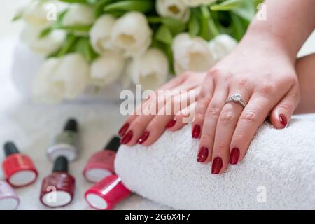 Primo piano delle mani di una giovane donna con chiodi rossi lucidati e strass applicati in un salone di bellezza alla moda Foto Stock