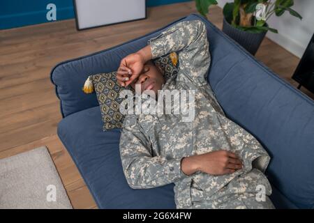 Uomo in camuffamento con occhi chiusi sul divano Foto Stock
