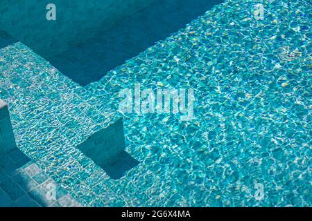 Superficie d'acqua ondulata della piscina con scale e bordi della piscina. Concetto di vacanza soleggiata o di vacanza Foto Stock