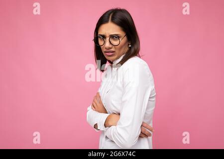 Bella giovane offesa triste donna bruna indossare tutti i giorni abiti eleganti e moderni occhiali ottici isolati sulla colorata parete di sfondo guardando Foto Stock