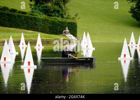 L'artista Steve Messam file una barca tra le sue opere d'arte, Drifted - 12 piramidi galleggianti nel canale, con l'ispirazione di una follia piramidale perduta, che fa parte dell'installazione artistica di Messam "These Passing Things" presso Fountains Abbey e Studley Royal, vicino Ripon. Data immagine: Venerdì 9 luglio 2021. Il credito fotografico dovrebbe essere: Owen Humphreys/PA Wire Foto Stock