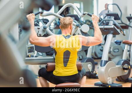 Vista posteriore di un potente allestitore con braccia forti che si esercitano durante la routine di allenamento del corpo superiore in un centro fitness con attrezzature moderne Foto Stock