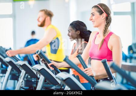 Vista laterale di montare una donna felice e il suo gruppo di allenamento su tapis roulant in palestra Foto Stock