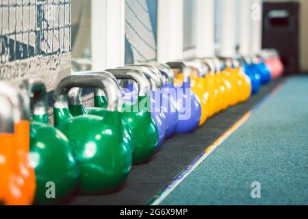 Primo piano di kettlebells metallici di vari pesi e colori sul pavimento di un centro fitness con attrezzature moderne per l'allenamento funzionale Foto Stock