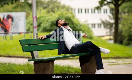 Giovane uomo colloquiale all'aperto - seduto fuori su una panchina nel parco - natura Foto Stock