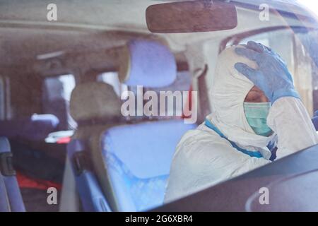 Un paramedico esausto in indumenti protettivi fa una pausa nell'ambulanza durante la pandemia del coronavirus Foto Stock