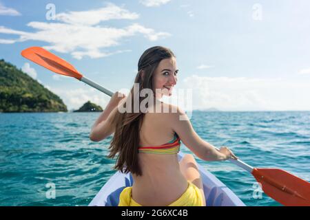 Vista posteriore di una giovane donna paddling con un doppio-bladed pagaiare in canoa sul mare durante le vacanze estive in sull isola di Flores, Indonesia Foto Stock