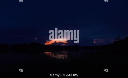 Ultimi momenti di un bellissimo e magico tramonto sul lago con nubi ricci in estate e il riflesso della luce sull'acqua Foto Stock