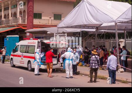 Phnom Penh, Cambogia. 9 luglio 2021. Per 4 mesi Phnom Penh sta combattendo contro un picco COVID - 19. Cambogiani, in maschere protettive viso / coperture, che hanno testato positivo per il virus attendere per entrare in un'ambulanza, con le loro borse imballate, in un sito di test di massa. 2 EMT / medici in pieno DPI controllare la situazione portando un vecchio cambogiano, senza toccarlo, in ambulanza. I cambogiani che provano positivi non possono lasciare il sito di test e hanno bisogno di chiamare un amico o un parente per ritirare i loro effetti personali per il soggiorno di 2 settimane in un ospedale. Credit: Kraig Lieb / Alamy Live News Foto Stock