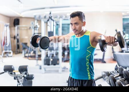 Ritratto di un bel giovane uomo determinato che si esercita con manubri durante la routine di allenamento del corpo superiore in un moderno fitness club Foto Stock