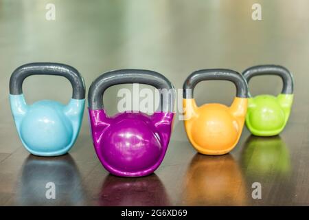 Primo piano di quattro kettlebells di diversi colori e pesi per un allenamento funzionale intenso che si riflette sul pavimento di un moderno fitness club Foto Stock