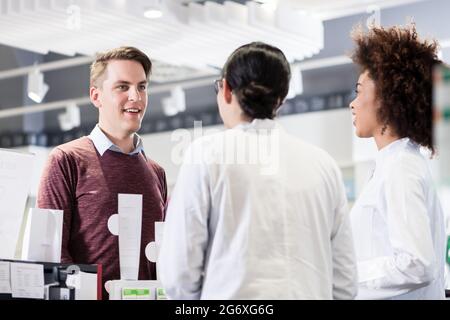 Allegro giovane e felice il cliente a parlare con due utili femmina di farmacisti in farmacia in contemporanea con personale gentile Foto Stock