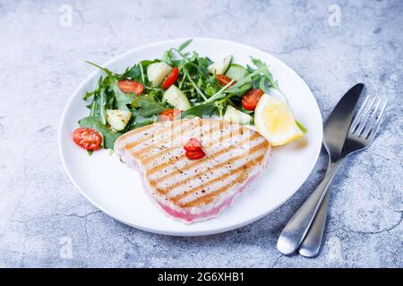 Bistecca di tonno alla griglia con verdure fresche, rucola, spinaci e limone. Primo piano. Foto Stock