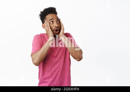 Scioccato ragazzo afro-americano gazzare, gridare e guardare spaventato in alto a destra angolo, frustrato da smth, spaventato di logo da parte, in piedi in t rosa Foto Stock
