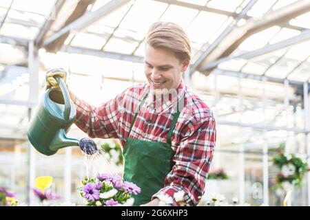 Esperto bel giovane irrigazione con cura e pazienza potted houseplants giallo mentre lavora come un fioraio in un moderno negozio di fiori Foto Stock